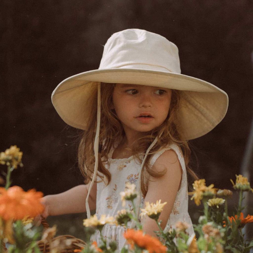 Little girl picking flowers wearing white kids bucket hat