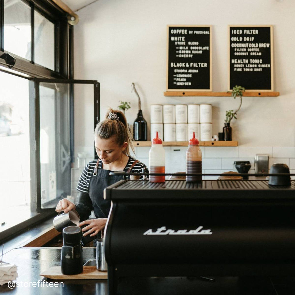 A barista is pouring coffee behind an espresso machine in a cafe