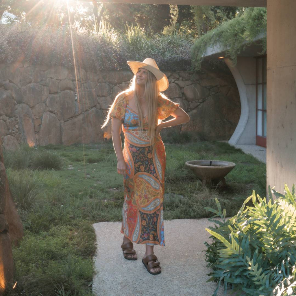 Woman with long blonde hair wearing a cowboy hat standing in front of ground house 107r