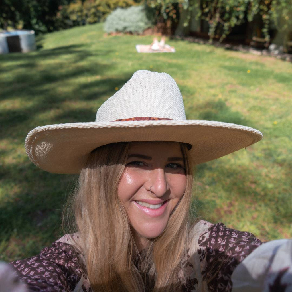 A close up photo of a woman with long blonde hair wearing a straw cowboy hat, she is smiling at the camera