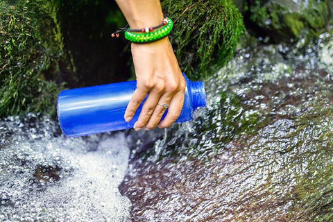 hiker filling up water bottle with fresh water outside