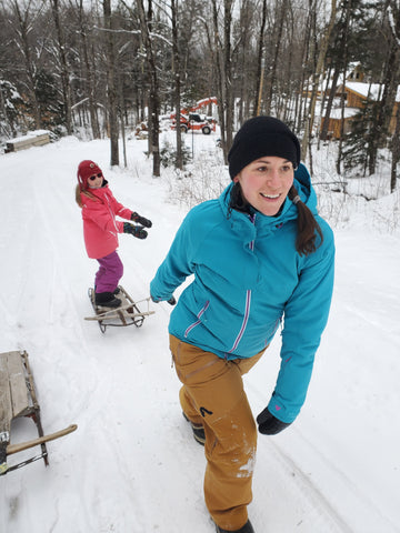 Devin and Kayah sledding while devin is wearing her upcycled rubber adventure ABD jewelry.