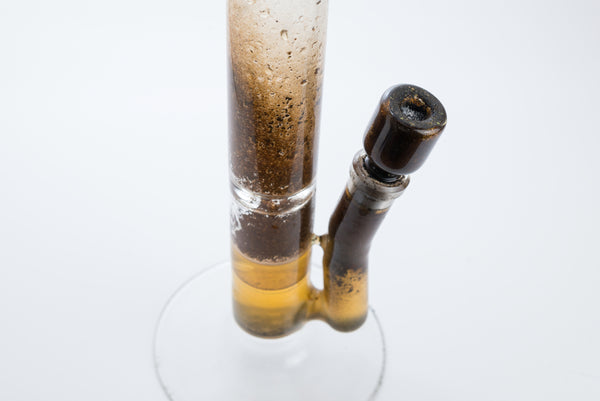 A close up of a dirty bubbler, with yellow water and clear glass base.