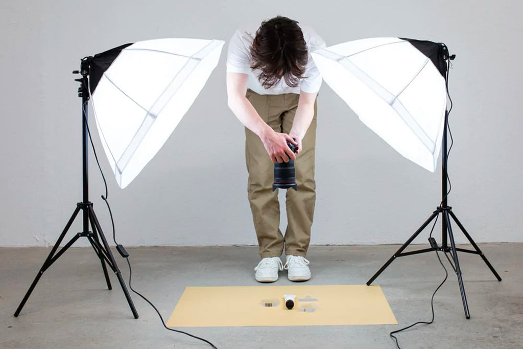 Male photographer bent over taking a photo of a beige flat lay with octagon softboxes on either side of him