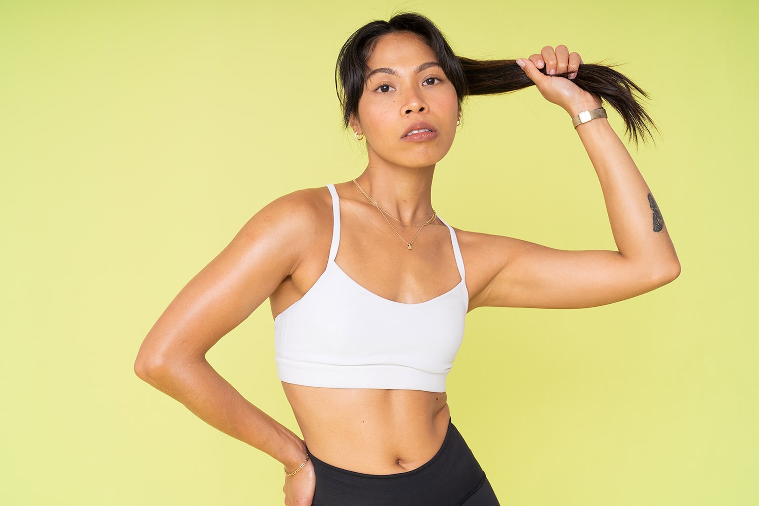 Half-length shot of a model wearing gym attire against a vibrant Spectrum Lemon Lime Splice Green Paper backdrop. The model is holding her ponytail, demonstrating a moment of active movement.