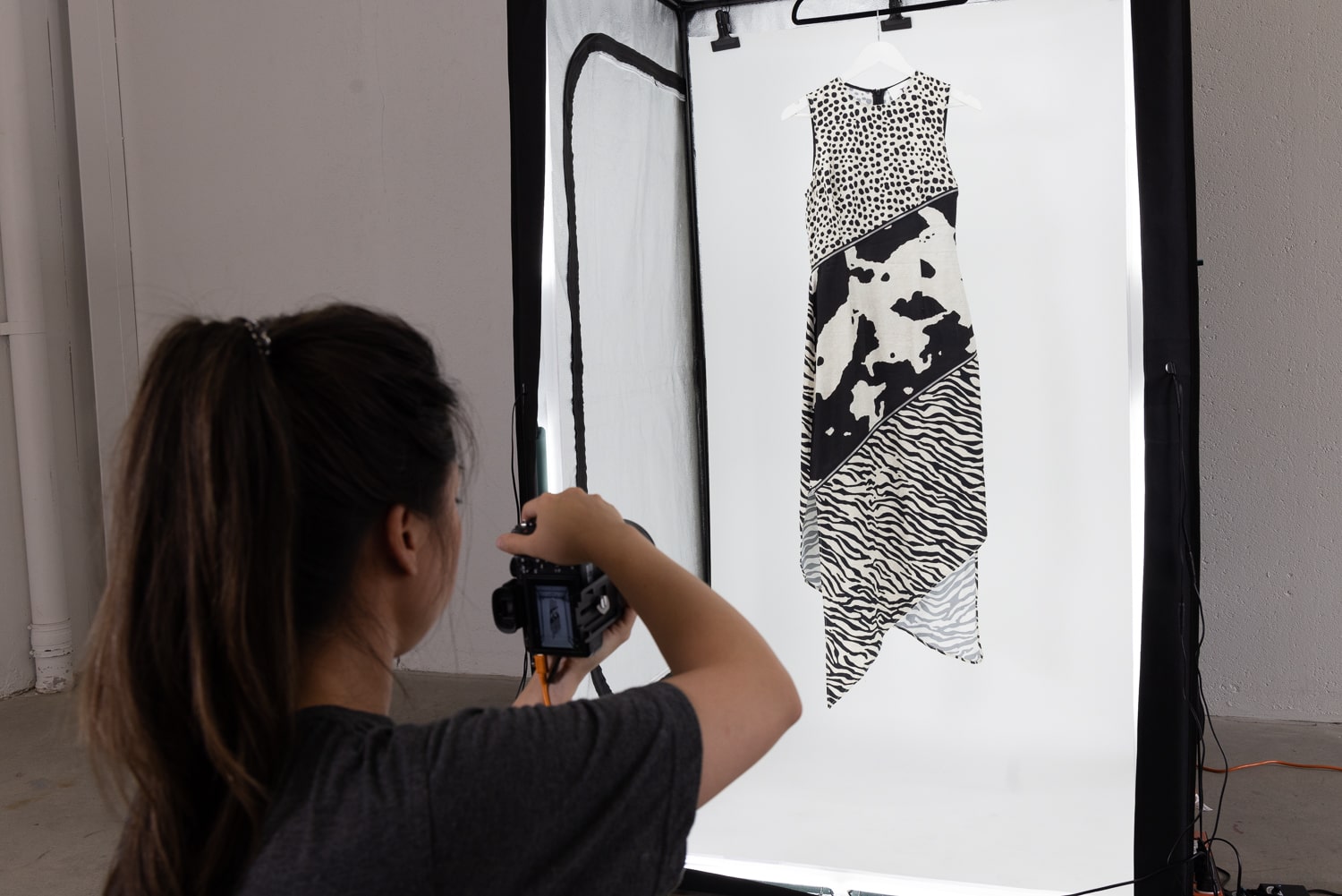 An image of a photographer capturing a photo of a black and white animal print dress that is hanging from a hook. The dress is the focal point of the imageAn image of a photographer capturing a photo of a black and white animal print dress that is hanging from a hook. The dress is the focal point of the image.