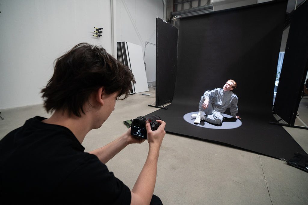 Male photographer taking photos of a male model sitting on a black backdrop