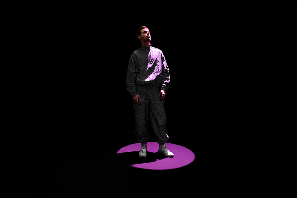 Male model in front of a black backdrop lit up by a purple spotlight