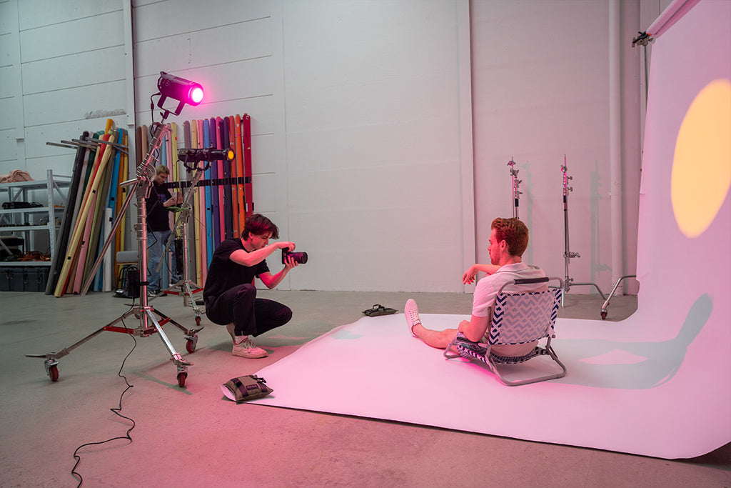 Male photographer taking photos of a male model sitting on a light coloured backdrop