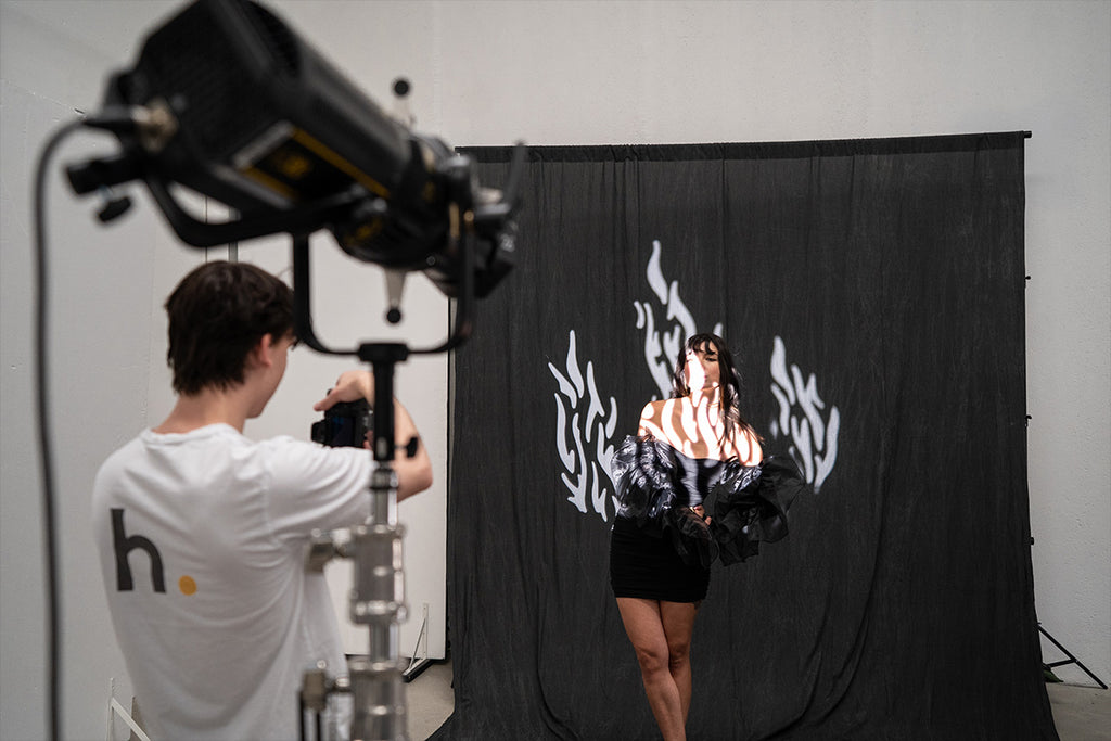 Male photographer taking photos of a female model in front of a black backdrop with a flame spotlight covering her body