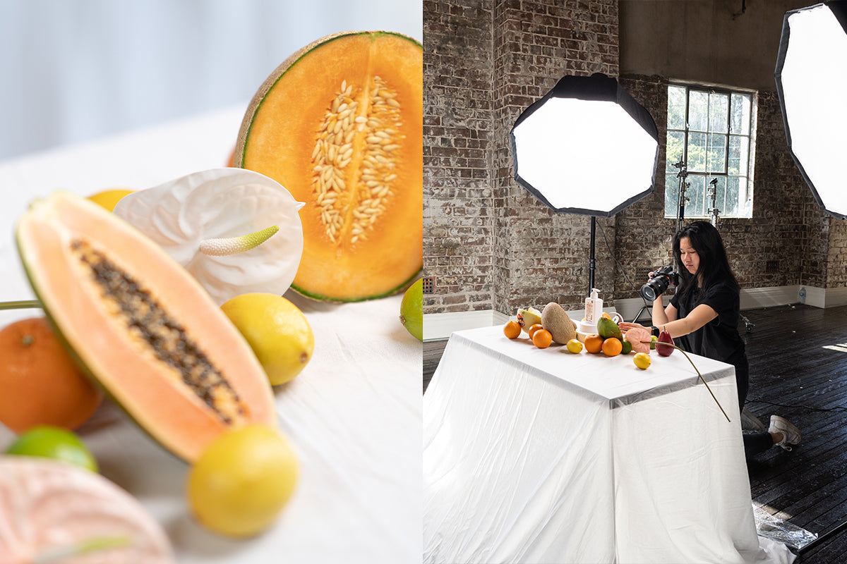 Left image: Fruit and flowers on a white muslin. Right image: Female photographer taking photos of fruit and flowers on a white muslin backdrop using two continuous lights with softboxes