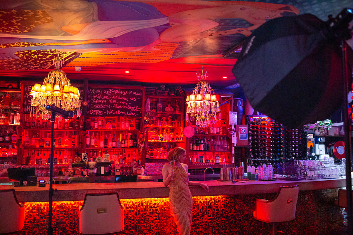 Woman holding a glass of champaign while leaning at the counter of an art deco style bar