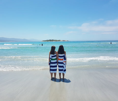 Two girls wrapped in beach towels looking at the ocean