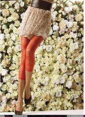Lady's legs in orange footless tights, floral skirt and black shoes, standing in front of a floral wall.