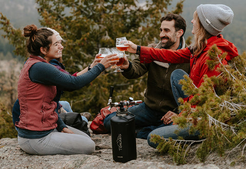 Friends enjoying craft beer from a TrailKeg Carbonated Growler while camping