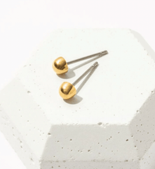 gold circular stud earrings. mini dome stud earrings on white brick background