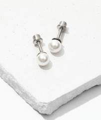 tiny hypoallergenic pearl earring with a titanium screw back on a white concrete background