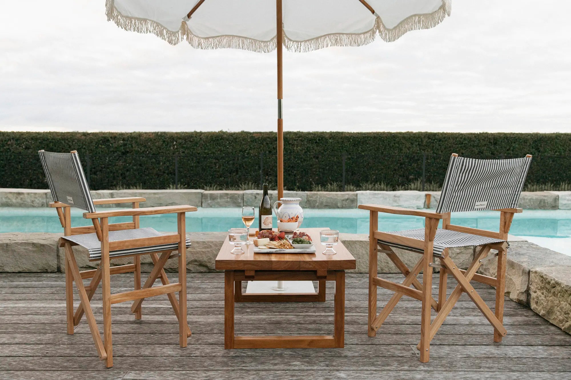 White umbrella, table and canvas navy stripes chairs on a pool deck