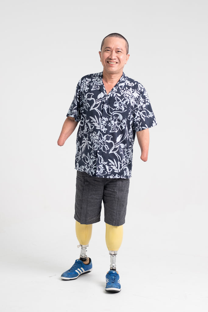Whee Boon, a 4-limb amputee, smiling at the camera as he donned the Tropical Short Sleeve Shirt in Navy and Unisex Adjustable Shorts in Shadow Grey.