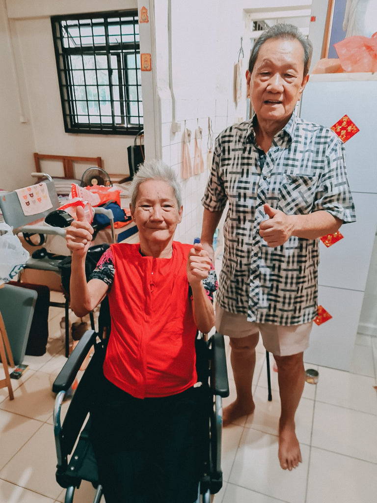 Mdm Tiah in her wheelchair and her boyfriend standing next to her, showing a thumbs-up after putting on the customised garments.