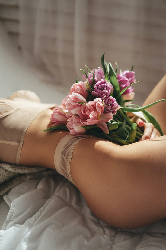 A woman is laying in her bra and panties with a bouquet of pink and purple flowers. 