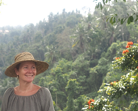 Eileen Holford founder of Wild Planet Aromatherapy in green dress with straw hat with trees behind in Bali 