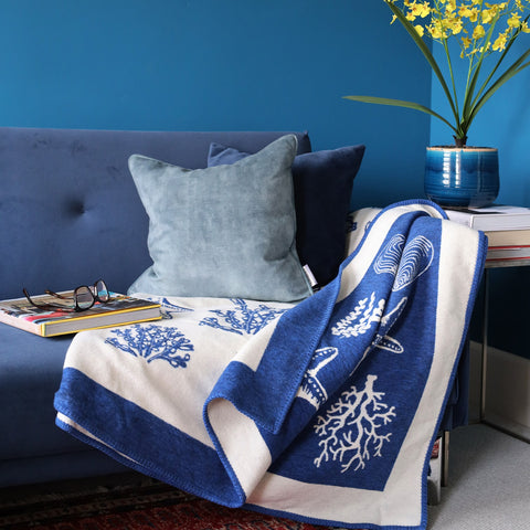 Velvet cushion and Cream Cornwall throw styled on a blue couch