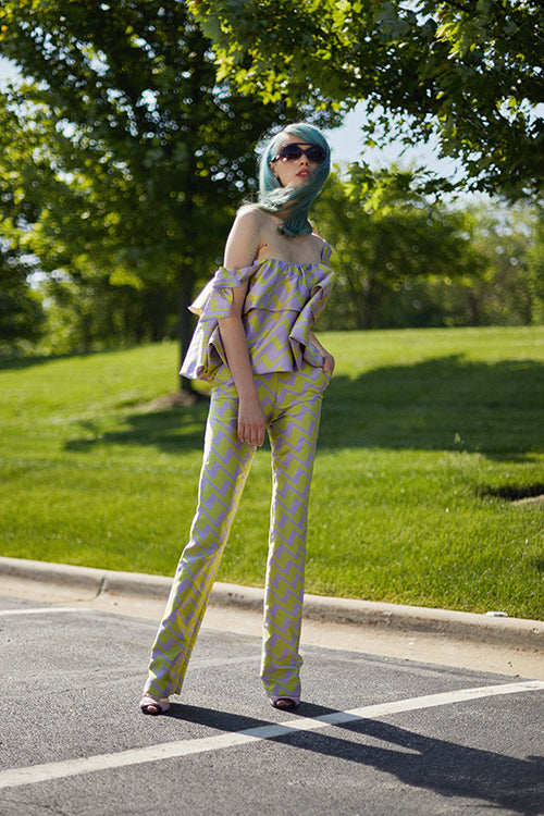 Cynthia Rowley Resort 2019 Collection features a patterned purple and green outfit, with fitted pants and a ruffled top with bows on the sleeves. 