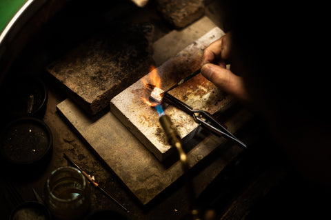 metalsmith/jewelry artist working at their bench with fire torch and metal.