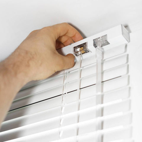 A hand adjusting the top of a white venetian blind