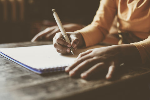 woman writing in journal on table in sunlight