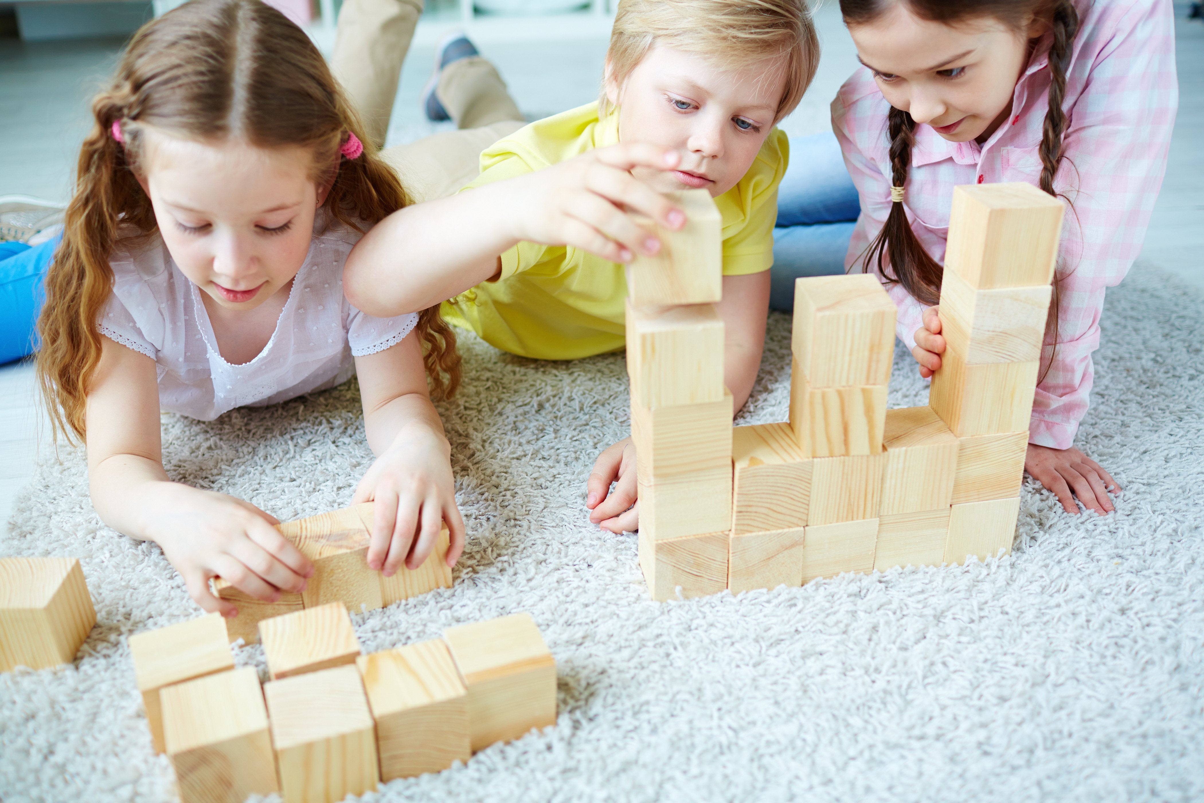  Three children are playing on the floor with wooden blocks and books.