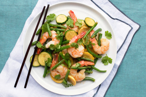 Close up of shrimp over green beans with zucchini, yellow squash, and cilantro.