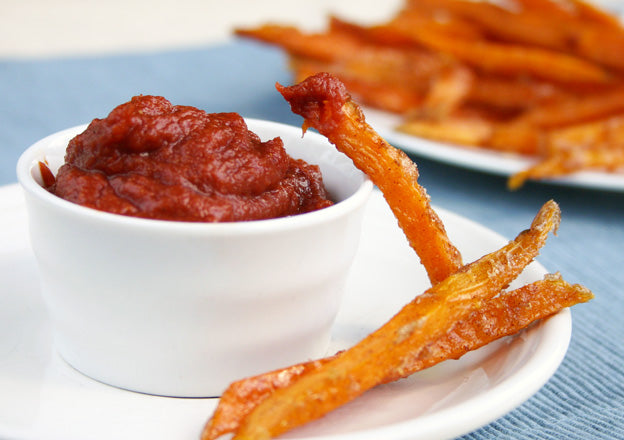 Ketchup in white bowl with sweet potato fries