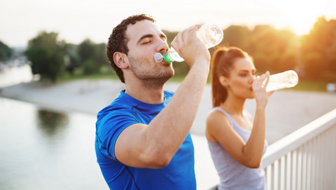 Man and woman drinking a bottle of water while on a run.