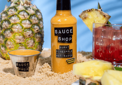 An image of Burnt Pineapple Hot Sauce in a summery, tropical scene