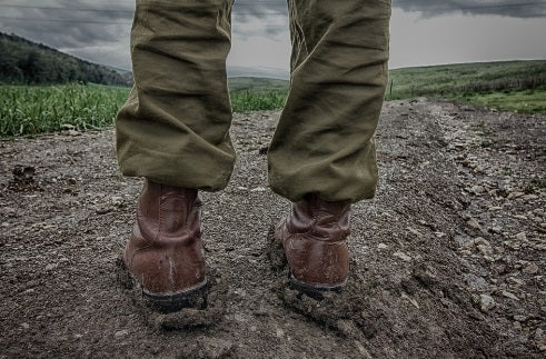 Pair of legs in brown boots standing in a rocky field