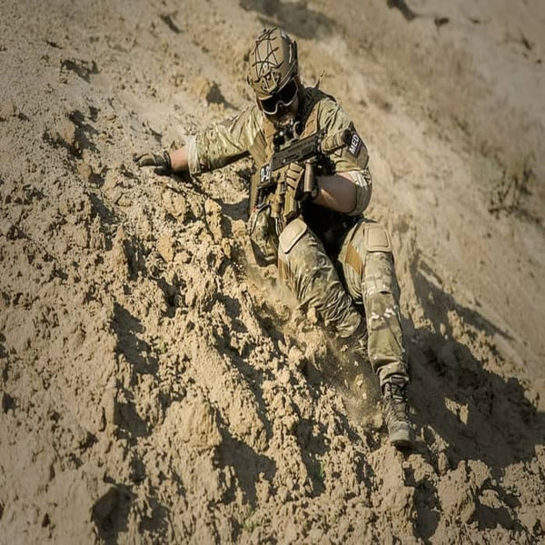 Soldier sliding off a rocky hill while carrying a rifle
