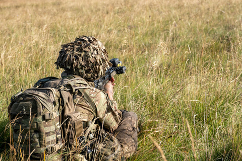 soldier in the field carrying a backpack, pointing weapon