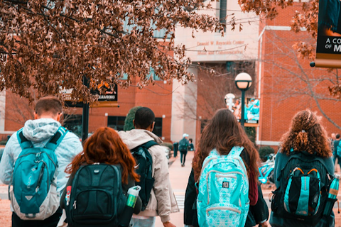 Five university students with backpacks walking into a campus building