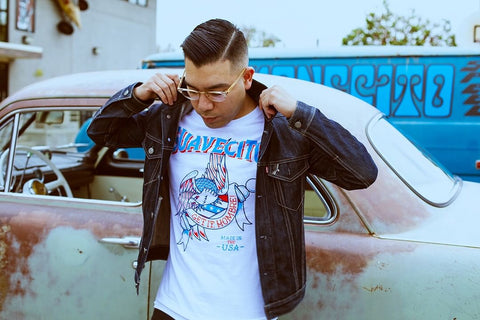 Man in a suavecito shirt outside of a classic car with hair done in a part. 