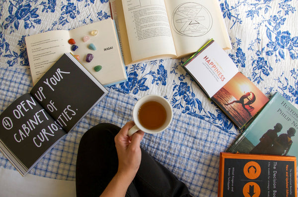 woman holding a cup of tea with a variety of gratitude books open on the floor