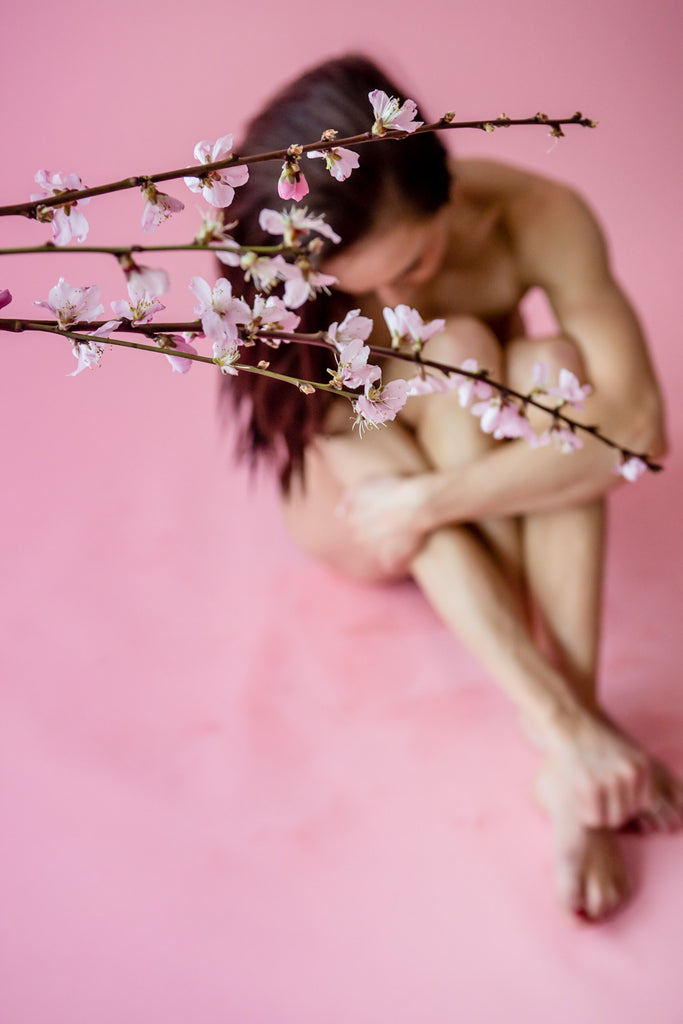 Nude Model Sitting Behind Pink Flowers on Pink Background