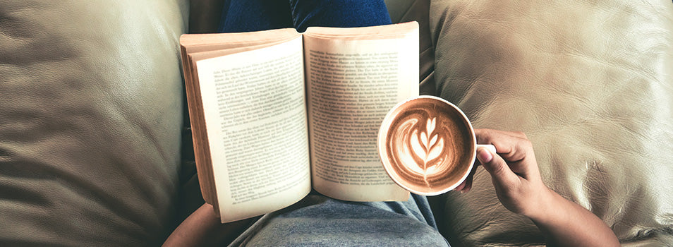 person reading a book with foamy coffee and the foam is shapped like a leaf