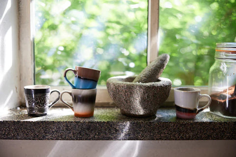 small espresso cups with ear in kitchen window next to glass jar with grounded coffee