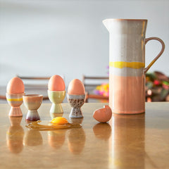sunny breakfast table setting with egg cups and a ceramic jug in pastel colors