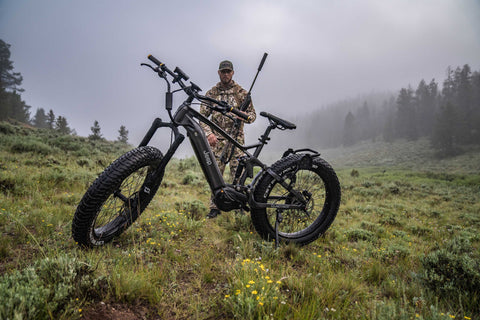 Jeep ebike in the woods with hunter standing behind the bike dressed in camo