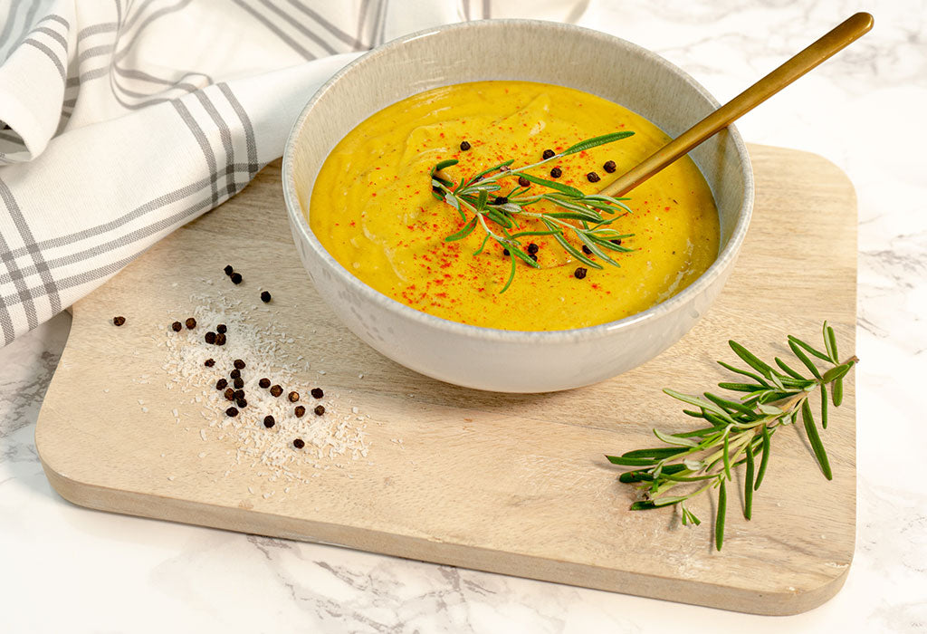 Eine gelbe Gemüsesuppe in einem gewölbten Teller auf einem Holzbrett