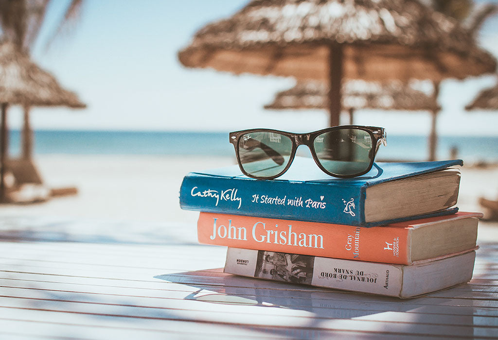 Bücher und Sonnenbrille am Strand unter einem Sonnenschirm