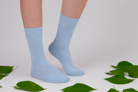 Light blue Hugh Ugoli socks worn standing among green leaves, emphasizing comfort and a connection with nature.